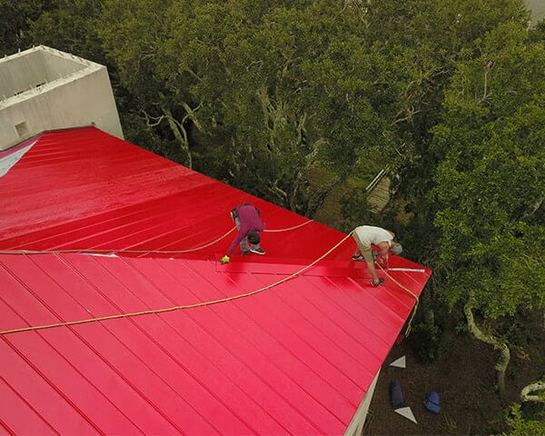 Crew on a red metal roof mid-installation, seen from above